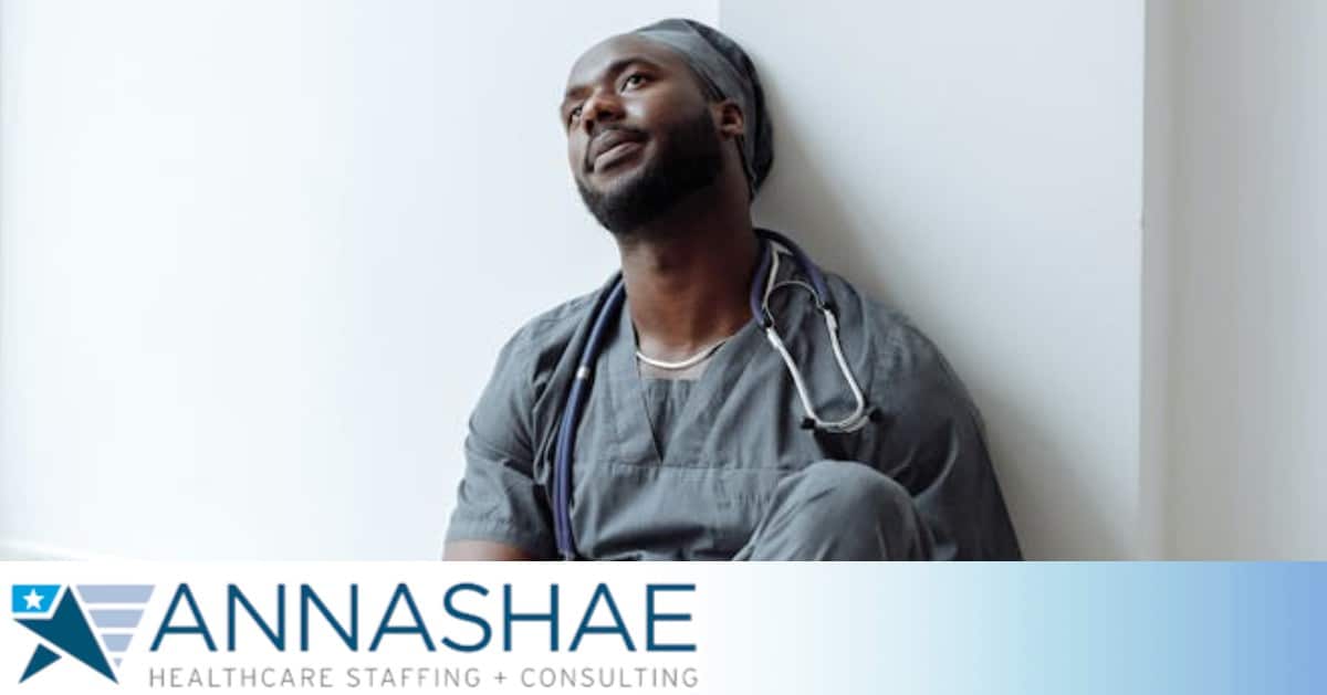 A healthcare professional experiencing stress in gray scrubs is resting against a wall, reflecting exhaustion.