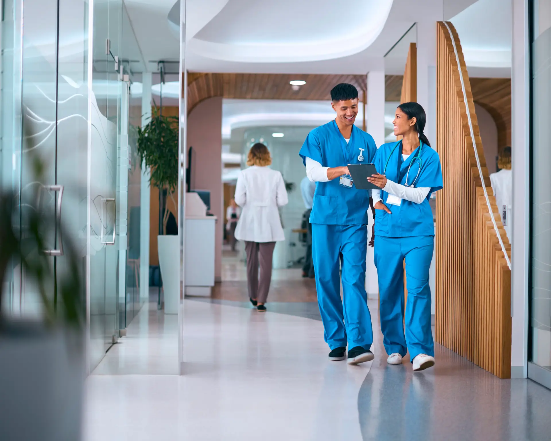Male And Female Doctors Or Nurses In Scrubs With Digital Tablet In Hospital With Colleagues Behind