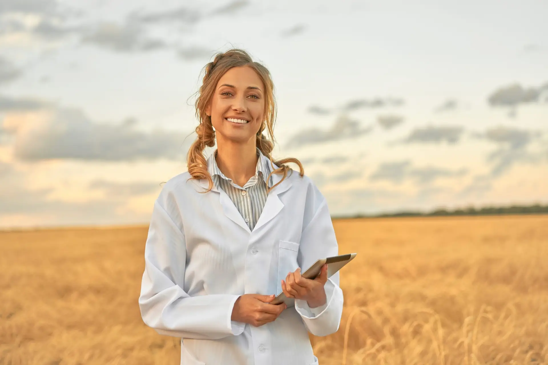 Woman farmer white coat smart farming standing farmland smiling using digital tablet Female agronomist specialist research monitoring analysis data agribusiness